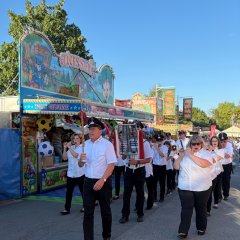 Spielmannszug Schöllenbachläuft auf Weg, im Hintergrund Jahrmarkt